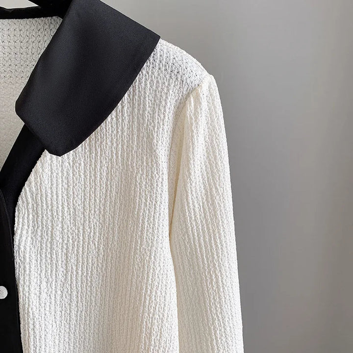 Weiße Strickjacke mit schwarzem Kragen, elegante Damenmode, Texturdetail.