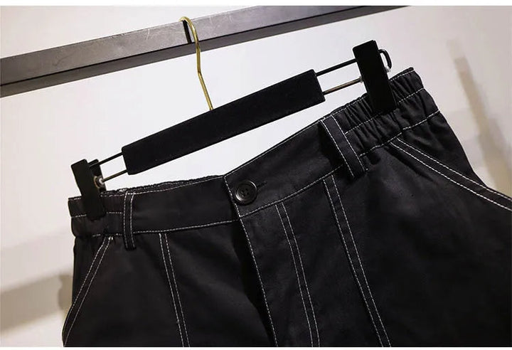 Schwarze Hose mit weißen Nähten, elastischer Bund, Knopfverschluss, auf Kleiderbügel.