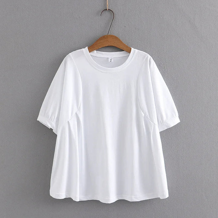 Weißes Damen-T-Shirt aus Baumwolle, kurzärmelig, auf Holzkleiderbügel vor grauer Wand.