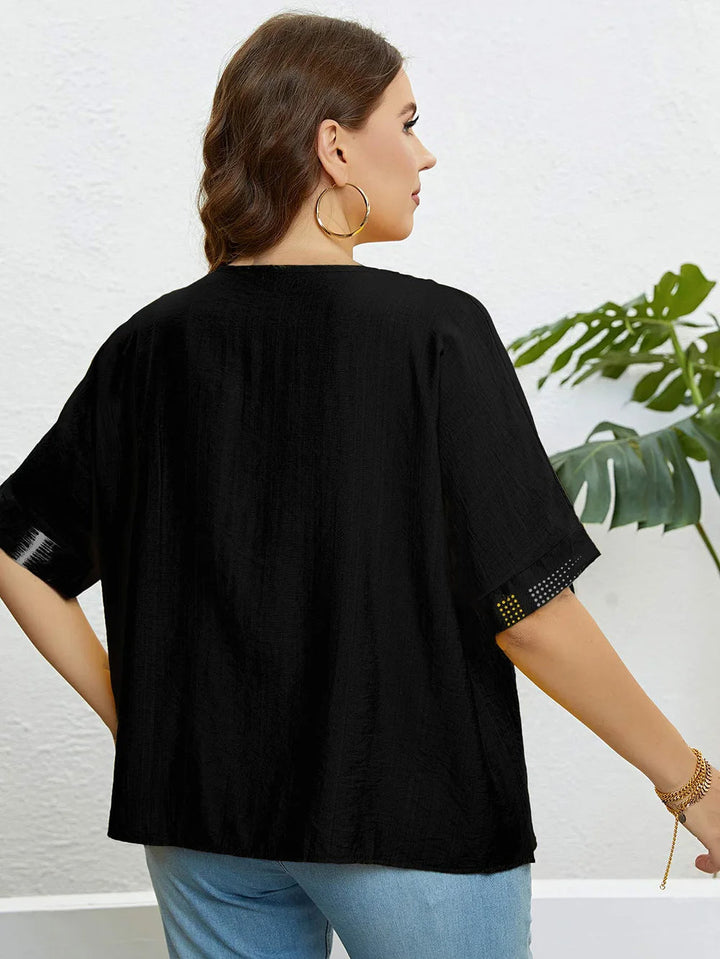 Frau in schwarzer Bluse mit kurzen Ärmeln, goldene Ohrringe, vor weißer Wand, grüne Pflanze.