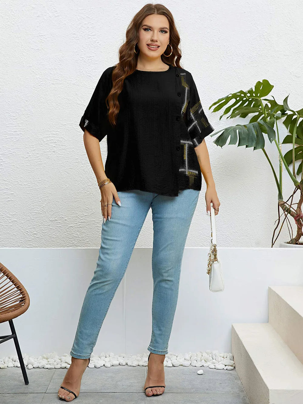 Frau in schwarzer Bluse und blauer Jeans, lässige Mode, Pflanzen im Hintergrund.