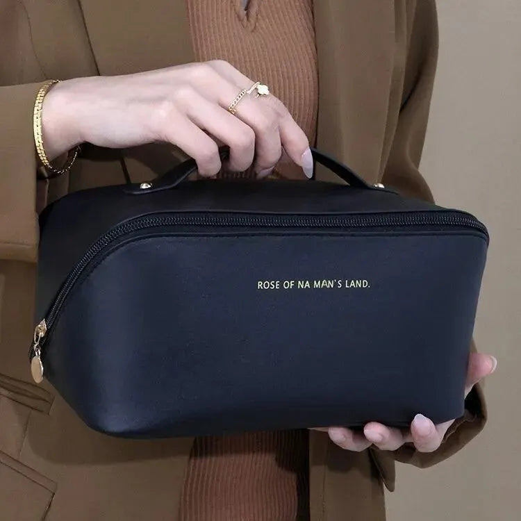 Schwarze Kosmetiktasche aus Leder mit Reißverschluss, gehalten von einer Person in brauner Kleidung.