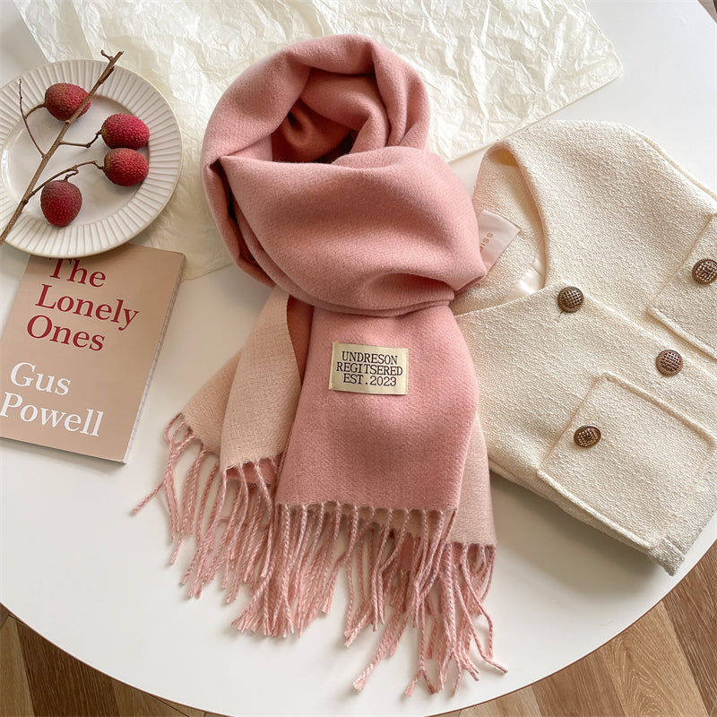 Rosa Wollschal mit Fransen auf Tisch, neben weißer Jacke und Buch, stilvolles Winteraccessoire.