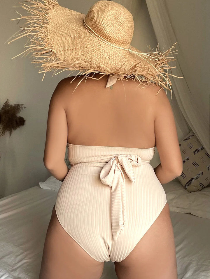Frau im cremefarbenen Badeanzug mit Strohhut auf Bett, Sommermode, Strandkleidung.