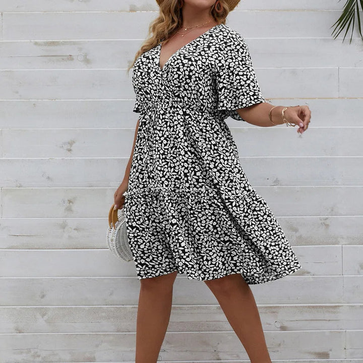 Frau in schwarz-weißem Sommerkleid mit Blumenmuster vor Holzwand.