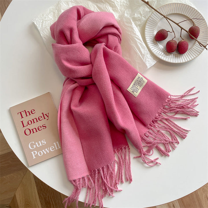 Rosa Kaschmirschal mit Fransen auf Tisch, neben Buch und Deko-Früchten, modisch und elegant.