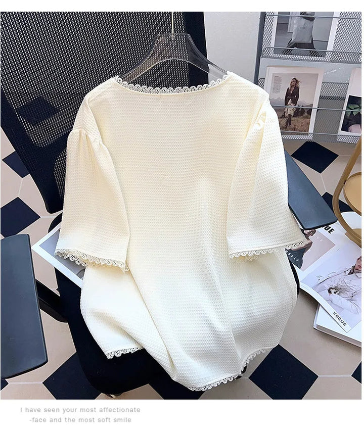 Weiße Damenbluse aus Baumwolle mit Spitzenbesatz, elegant, auf Bürostuhl drapiert.