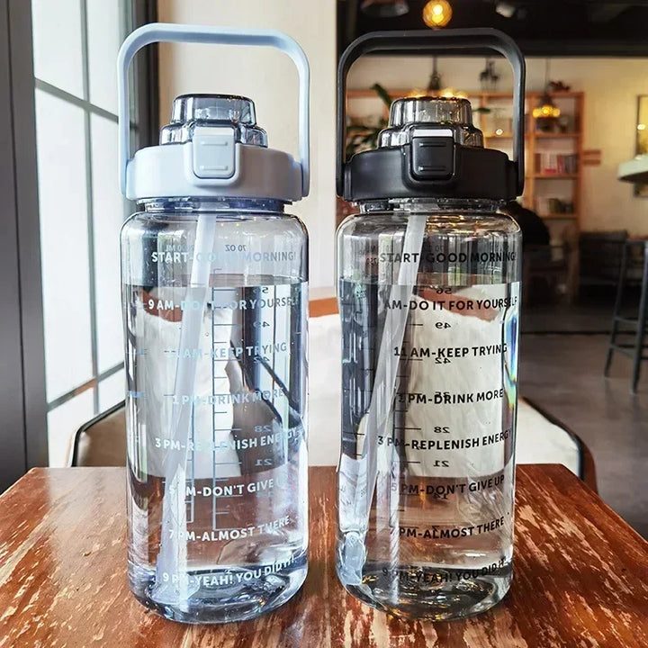 Zwei transparente Wasserflaschen mit Zeitmarkierungen, grauer und schwarzer Deckel, im Café.
