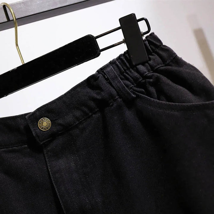 Schwarze Damenjeans aus Denim mit elastischem Bund und Knopfdetail auf Kleiderbügel.