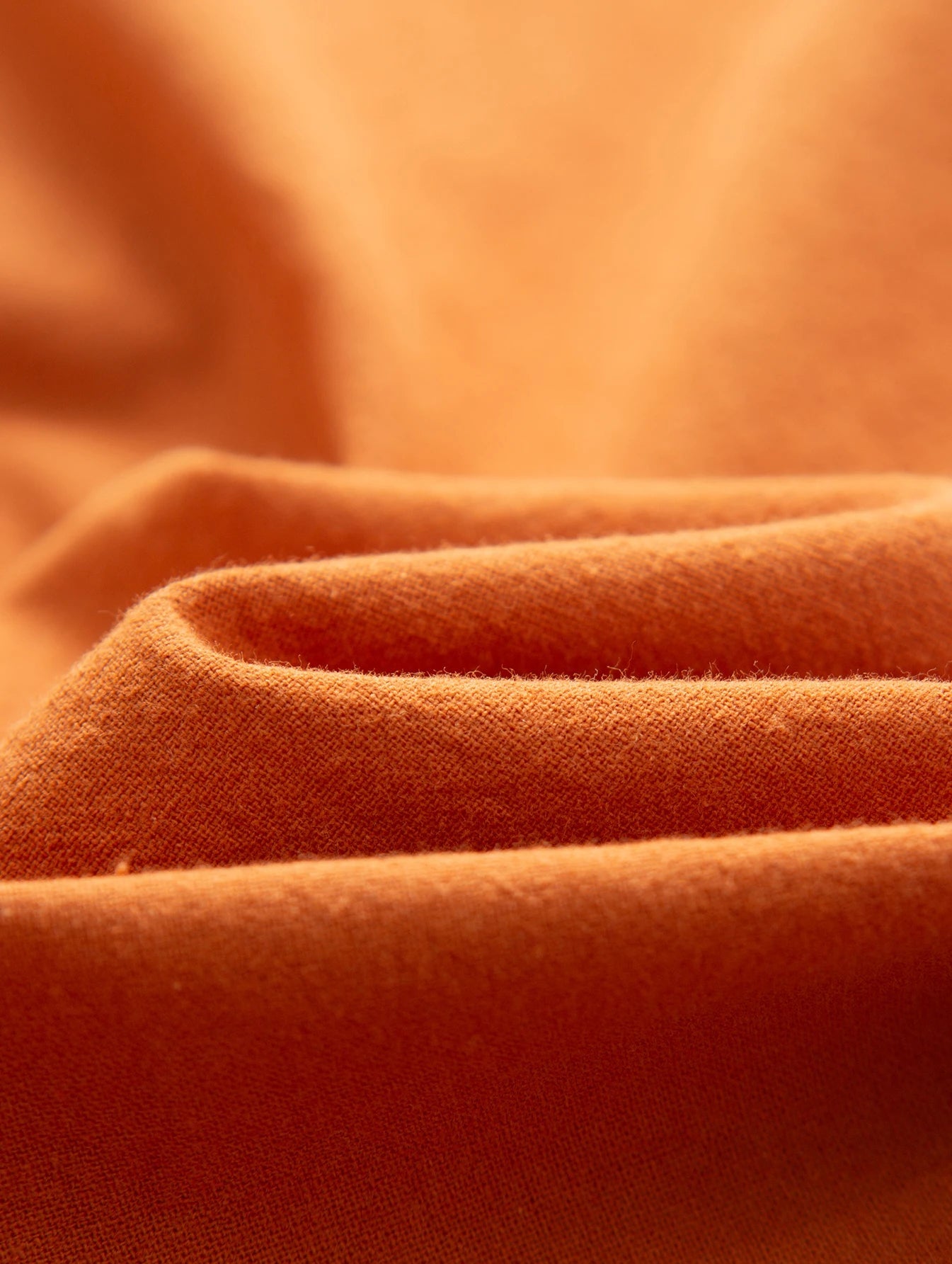 Orangefarbener Baumwollstoff, Nahaufnahme, weiche Textur, ideal für Bekleidung und Heimtextilien.