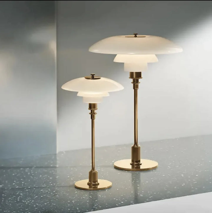 Zwei moderne Tischlampen aus Messing mit weißem Glasschirm auf glänzendem Tisch.