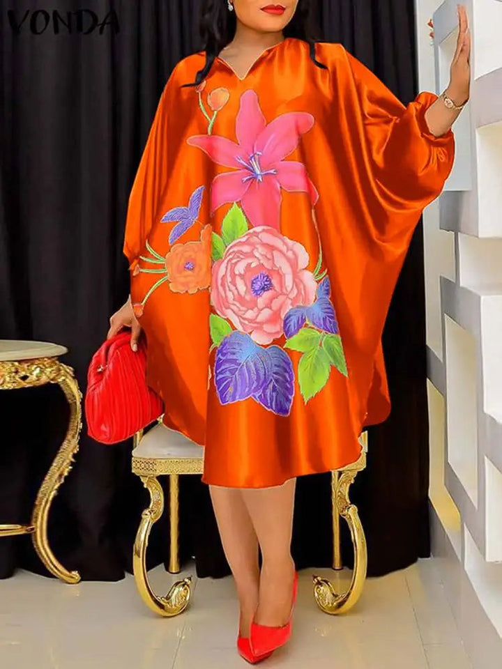 Frau in orangefarbenem Seidenkleid mit Blumenmuster, roter Tasche und Schuhen.