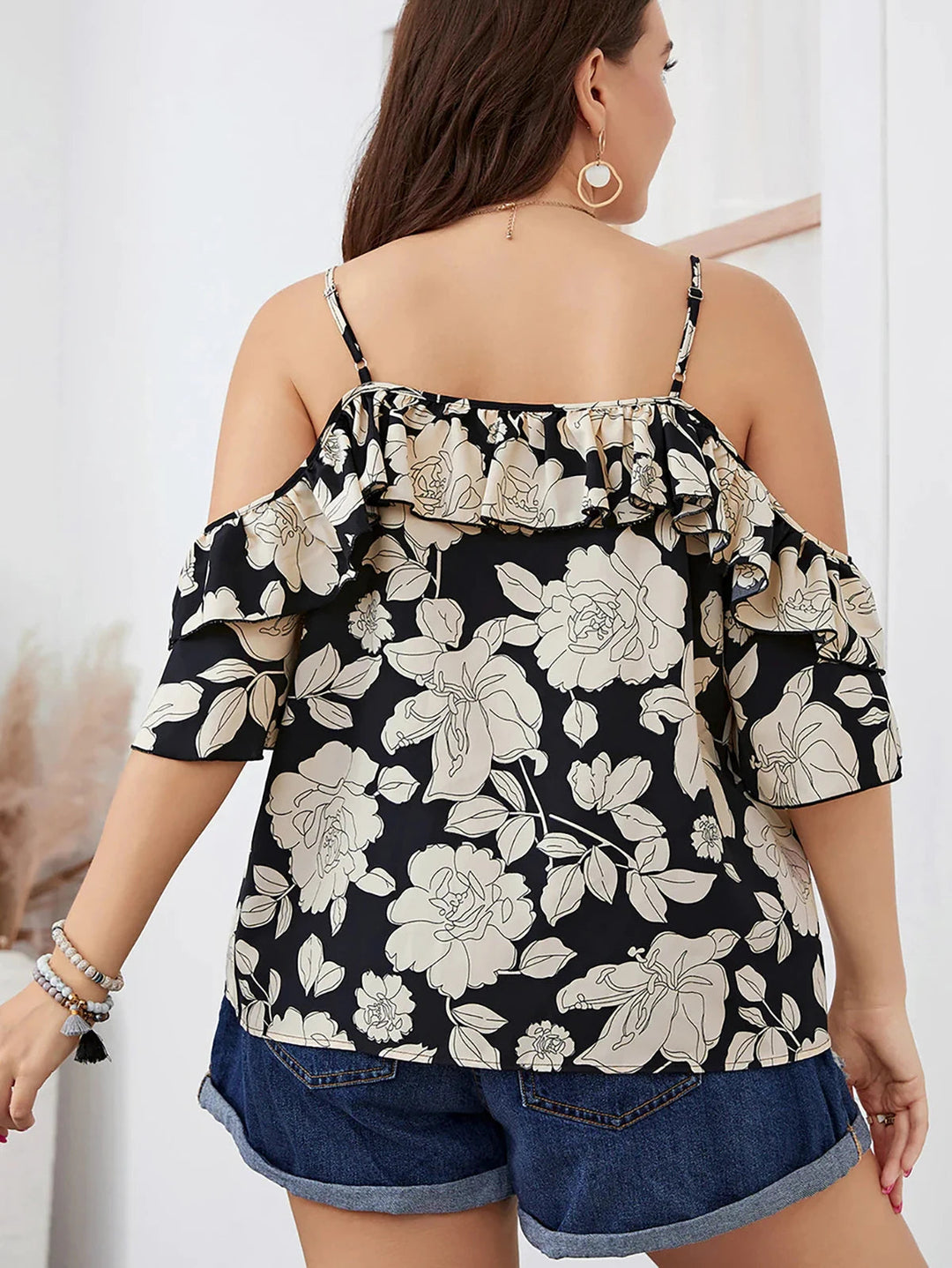 Frau in schwarzer, schulterfreier Bluse mit Blumenmuster und Jeansshorts von hinten.