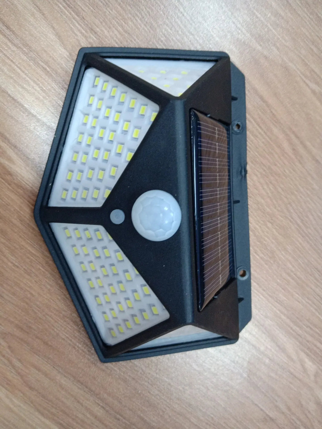 Schwarze LED-Solarleuchte mit Bewegungsmelder auf Holzoberfläche.