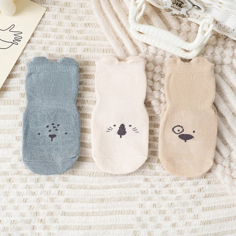 Drei Paar Baby-Socken mit Tiermotiven, blau, beige, creme, Baumwolle, auf Teppich.
