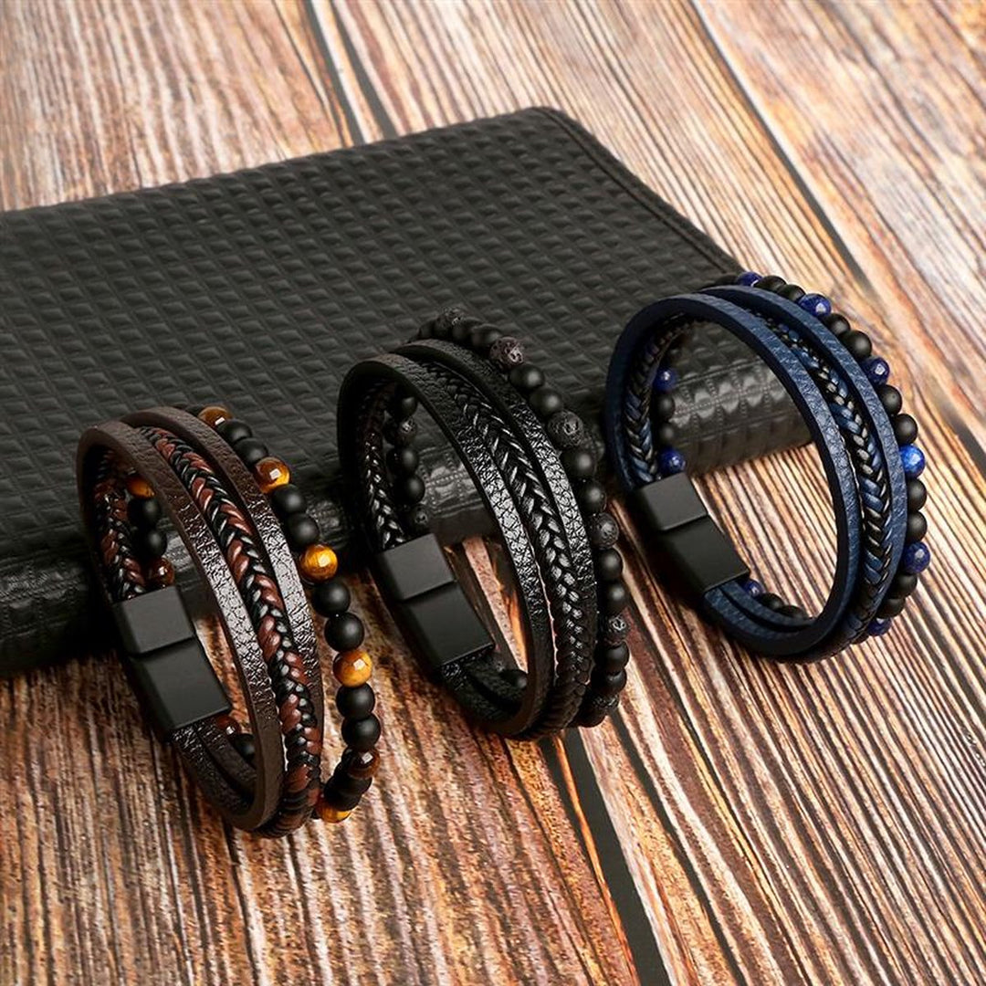 Drei geflochtene Lederarmbänder mit Perlen, schwarz, braun, blau, auf Holztisch.