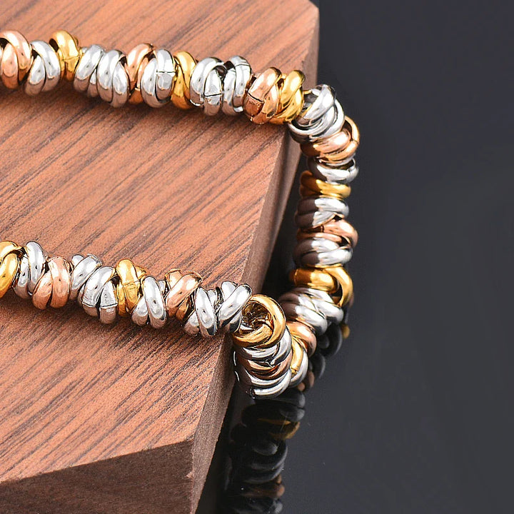 Dreifarbige Edelstahl-Armband, Gold, Silber, Roségold, auf Holz, modisches Schmuckstück.