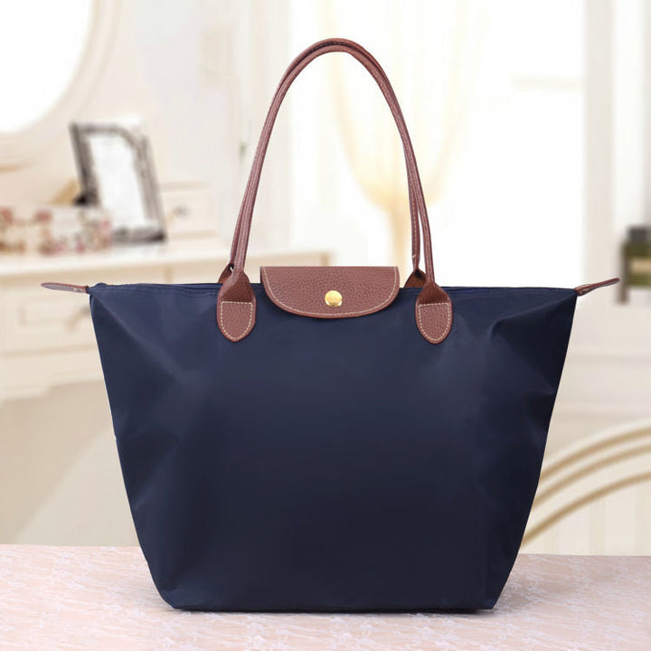 Dunkelblaue Handtasche aus Nylon mit braunen Ledergriffen auf Marmortisch.