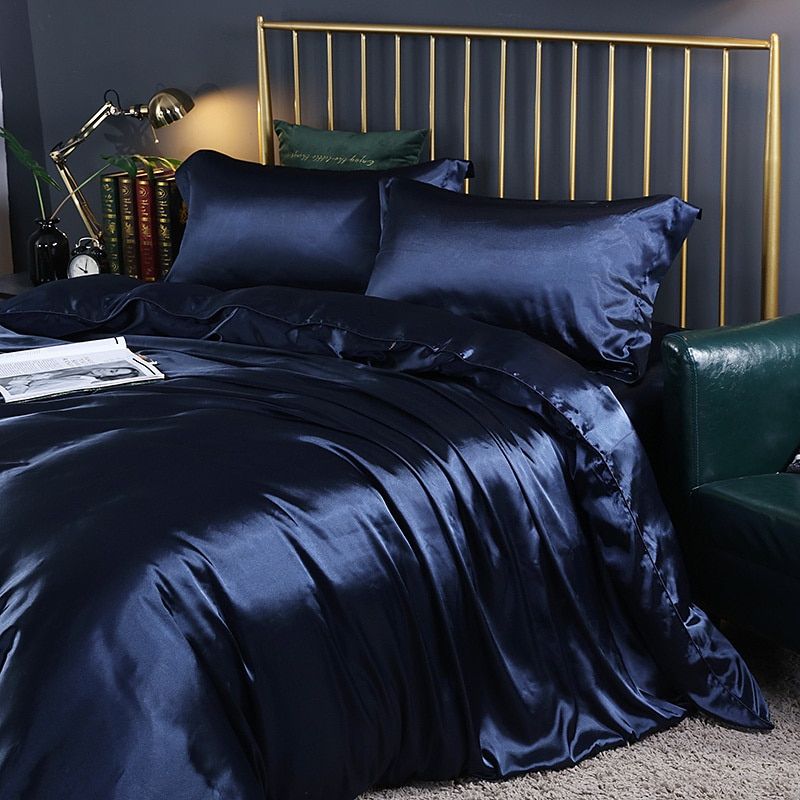 Dunkelblaue Seidenbettwäsche auf Bett mit goldfarbenem Kopfteil, luxuriöses Schlafzimmerdekor.
