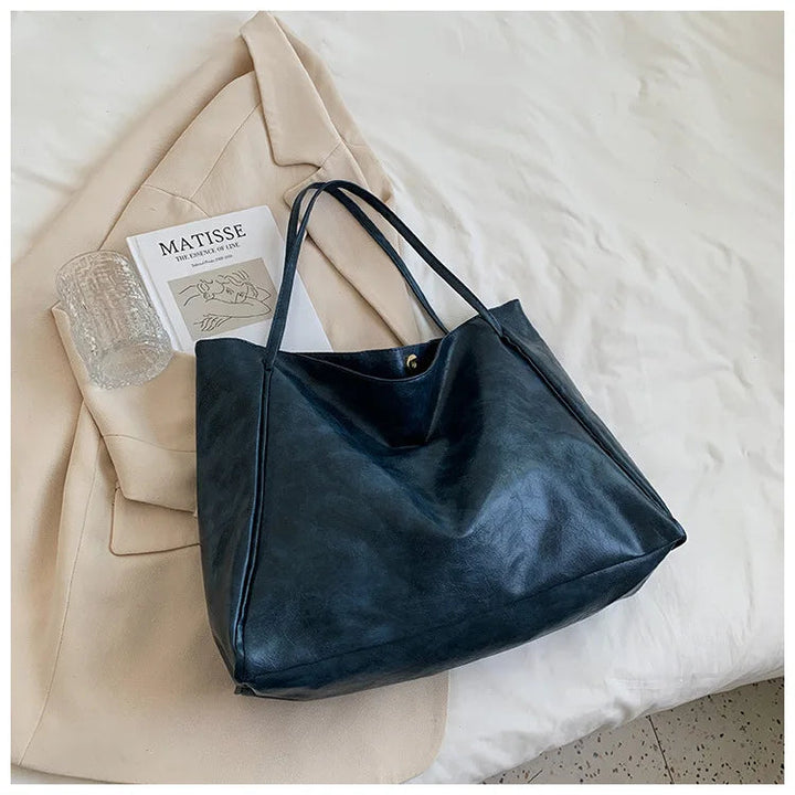 Dunkelblaue Ledertasche auf beigem Mantel, stilvoll, geräumig, modisch, Damenhandtasche.