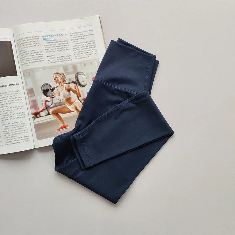 Dunkelblaue Sportleggings auf weißem Hintergrund neben offenem Fitnessmagazin.