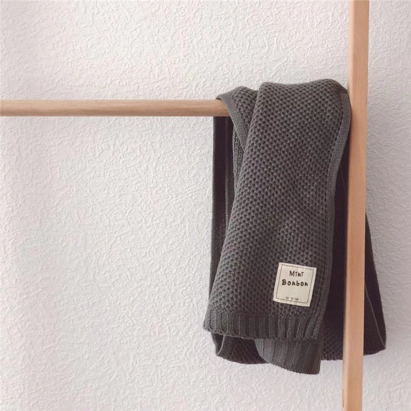 Dunkelgrauer Strickschal aus Baumwolle, hängend an Holzstange, modisch und warm.