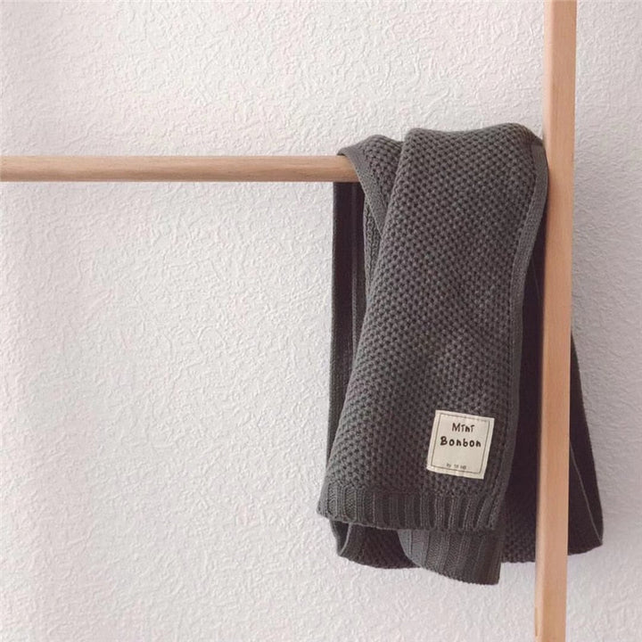Dunkelgrauer Strickschal aus Baumwolle, hängend an Holzstange, modisch und warm.