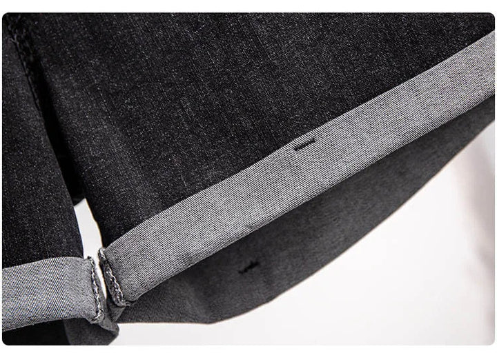 Dunkelgraue Jeansstoff-Detailaufnahme, umgeschlagener Saum, hochwertige Denim-Textur.