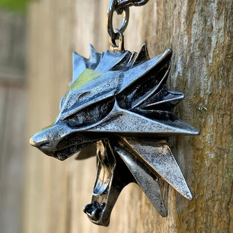 Silberner Wolfskopf-Schlüsselanhänger aus Metall, detailreich, an Holzwand hängend.