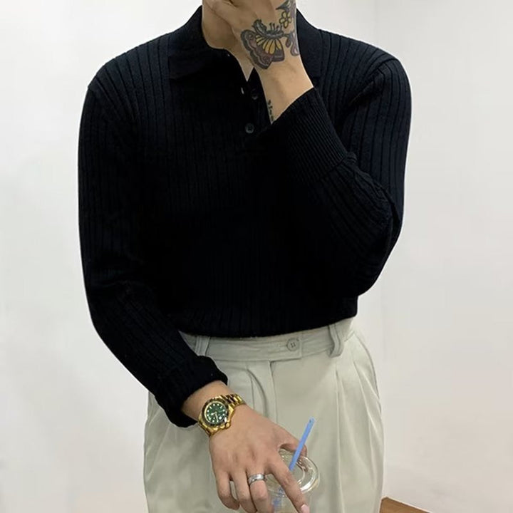 Mann in schwarzem Strickpullover, beige Hose, hält Getränk, trägt goldene Uhr, tätowierter Arm.