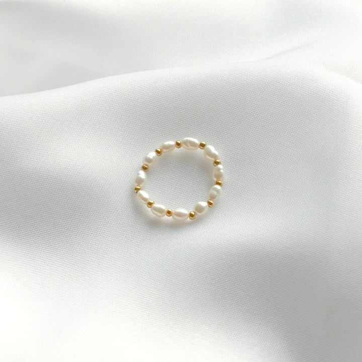 Echter Perlenring auf weißem Stoff, eleganter Schmuck, zeitloses Design, Damenaccessoire.