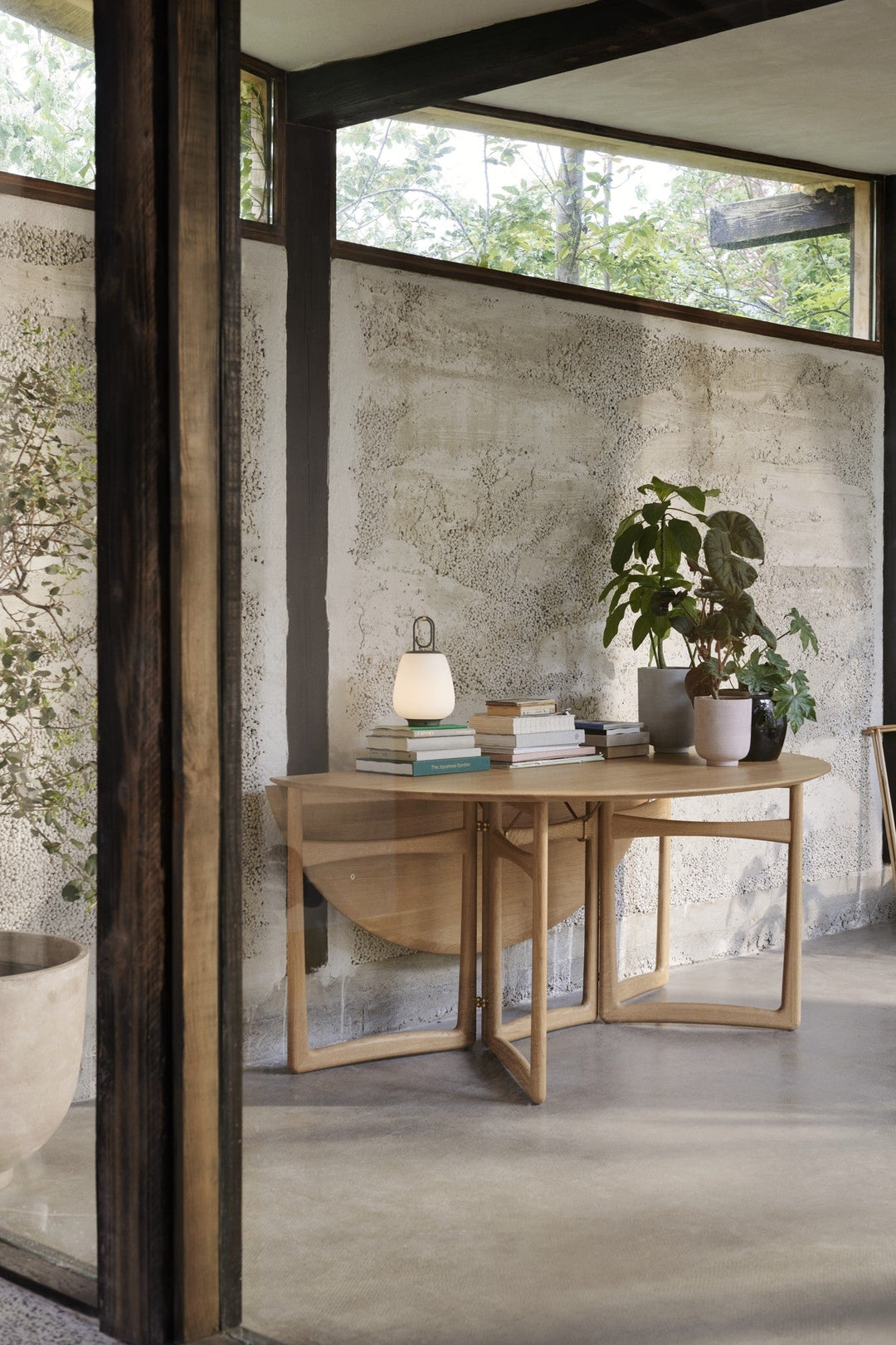 Holztisch mit Büchern, Pflanzen und Lampe in modernem Wohnzimmer, skandinavisches Design.