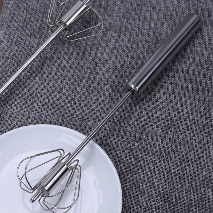 Edelstahl Handmixer auf grauem Stoff, neben weißem Teller, Küchengerät, langlebig, modern.