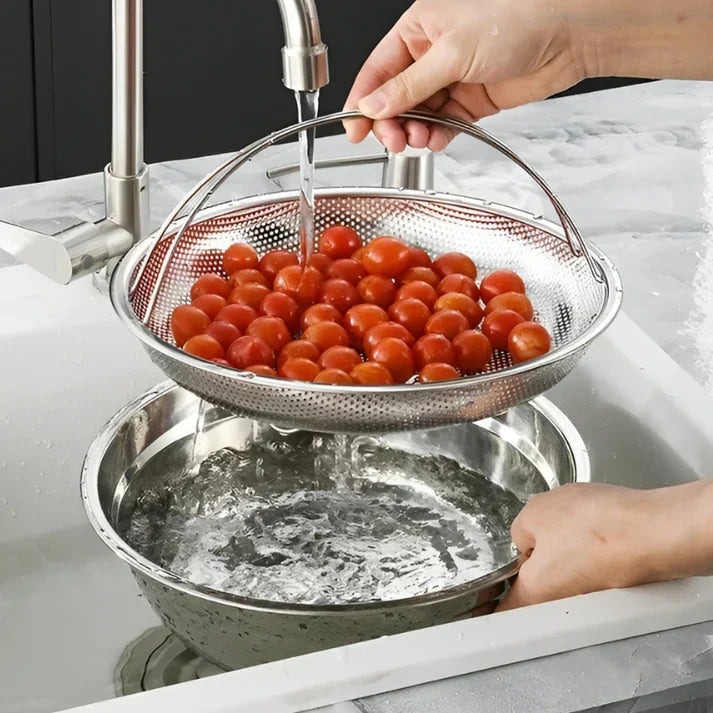 Hände waschen Kirschtomaten in Edelstahl-Sieb unter Wasserhahn in moderner Küche.