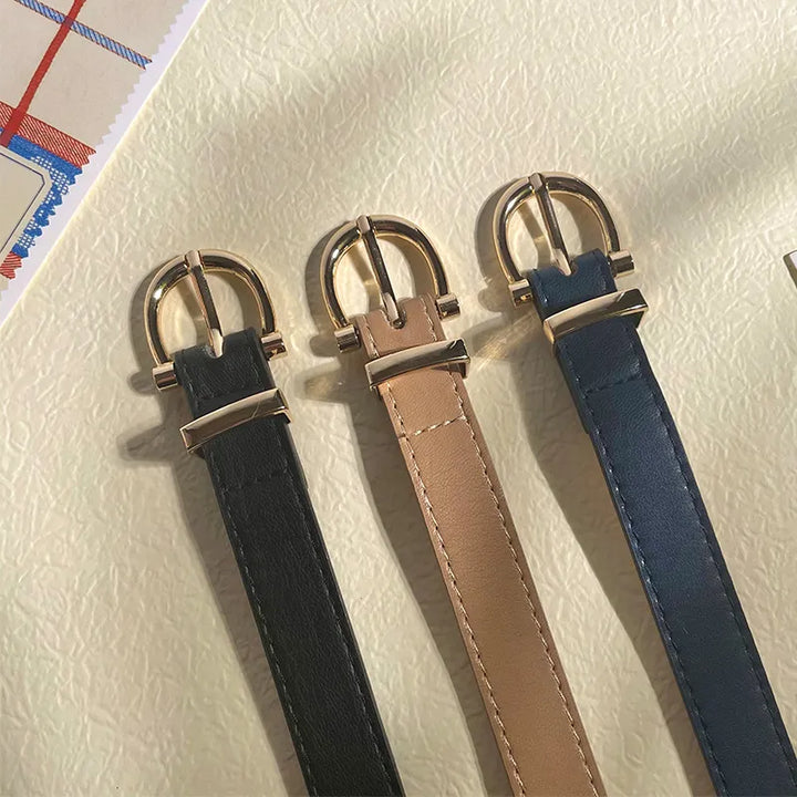 Drei Ledergürtel mit goldener Metallschnalle in Schwarz, Beige und Blau auf hellem Hintergrund.