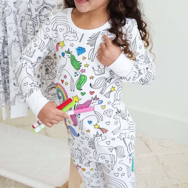 Mädchen in weißen Einhorn-Pyjamas mit Malstiften, aus Baumwolle, ideal für Kinder.