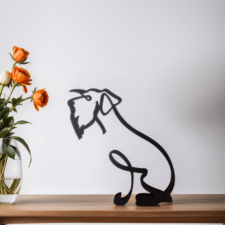Schwarze Hundeskulptur aus Metall auf Holzoberfläche neben Vase mit orangefarbenen Blumen.