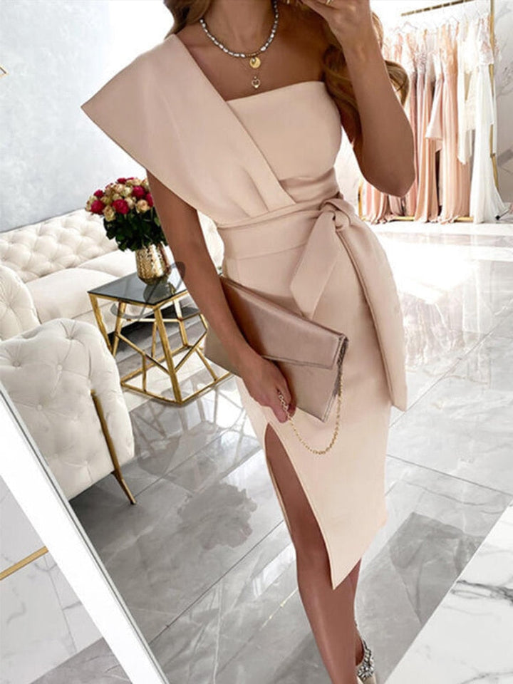 Frau in elegantem, cremefarbenem One-Shoulder-Kleid mit Schlitz, hält Clutch, luxuriöse Umgebung.