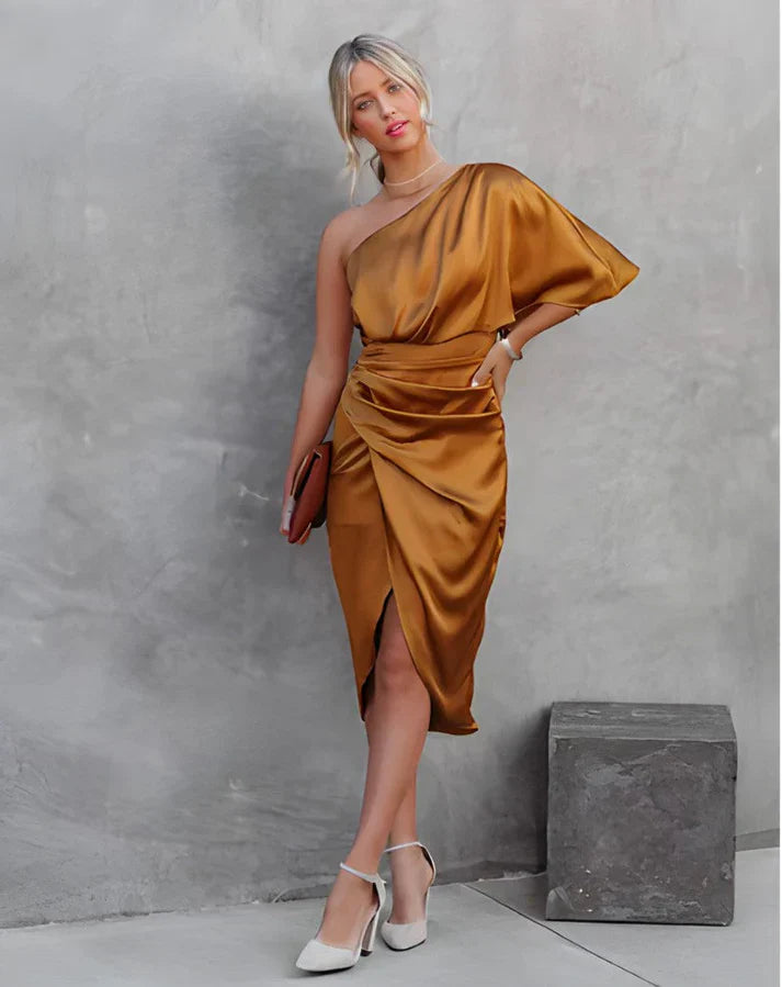 Frau in einem eleganten, goldenen, schulterfreien Seidenkleid mit asymmetrischem Schnitt.