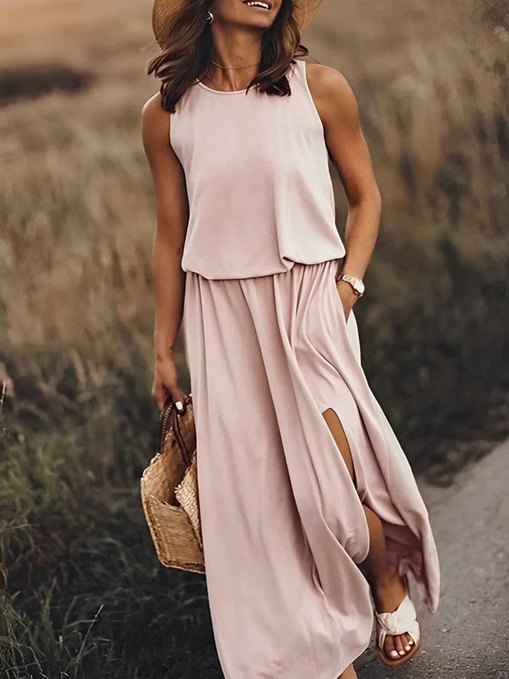 Frau in elegantem, ärmellosem, rosa Maxikleid mit Strohhut und Korbtasche auf Feldweg.