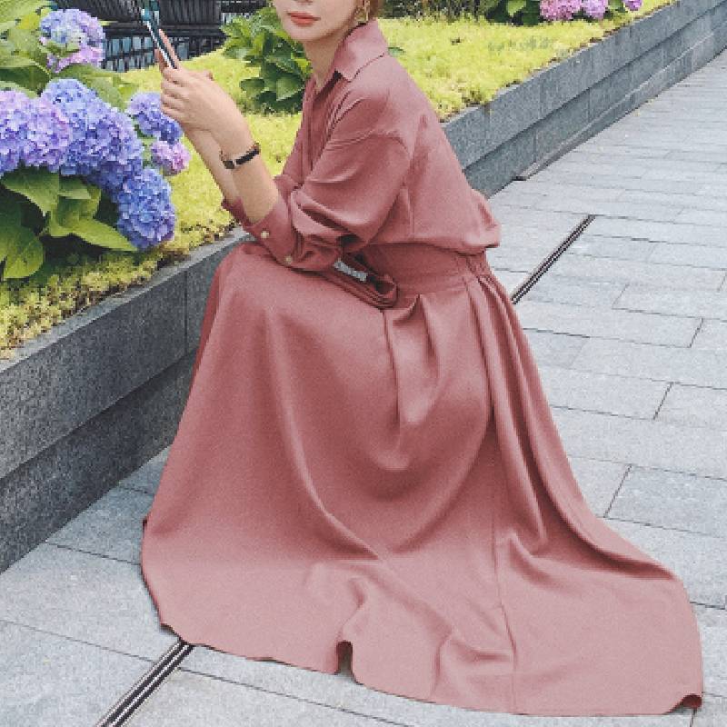 Frau in rosa Maxikleid sitzt neben Hortensien im Garten, elegantes Sommeroutfit.