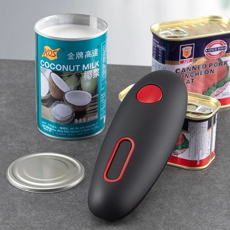 Elektrischer Dosenöffner schwarz-rot, neben Kokosmilch- und Fleischkonserven auf grauem Tisch.