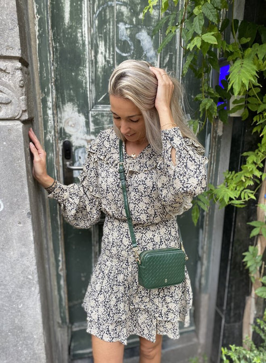 Frau in geblümtem Kleid mit grüner Umhängetasche vor antiker Holztür.