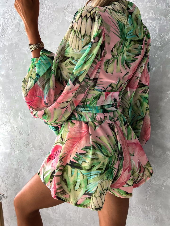 Frau in grün-rosa tropischem Kleid, lange Ärmel, Gürtel, Sommermode, floral, elegant.