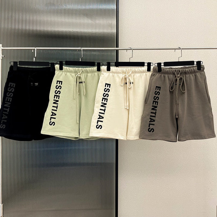 Vier Essentials-Shorts in Schwarz, Creme, Beige und Grau auf Kleiderstange.