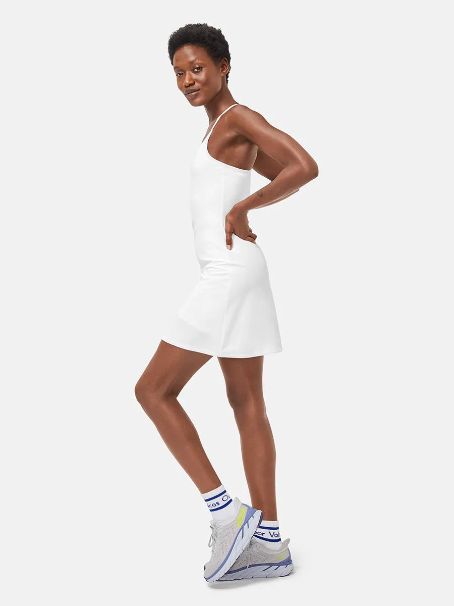 Frau in weißem Tennis-Kleid, seitlich, sportlich, lächelnd, mit grauen Sneakers und weißen Socken.