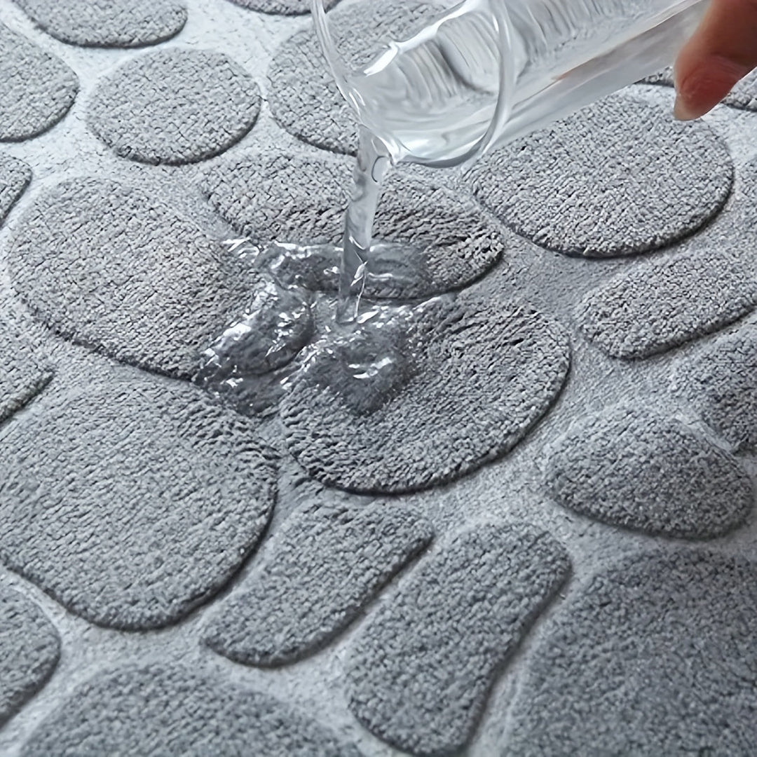 Grauer, wasserabsorbierender Badteppich mit Steinmuster, Wasser wird darauf gegossen.