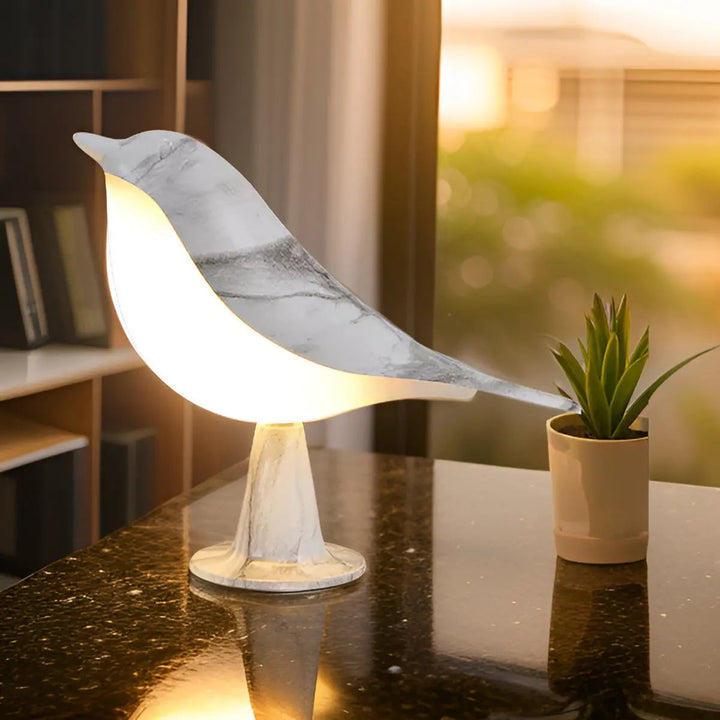 Leuchtende Vogel-Tischlampe aus Marmor auf schwarzem Tisch neben kleinem Kaktus, modernes Design.