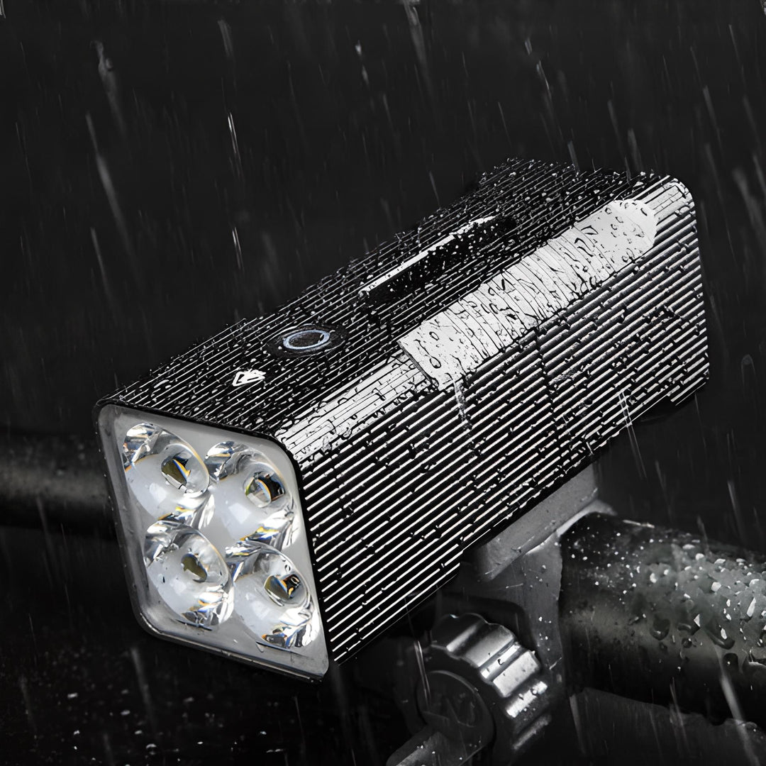 Wasserdichte LED-Fahrradleuchte, schwarz, mit vier Linsen, montiert auf Lenker im Regen.