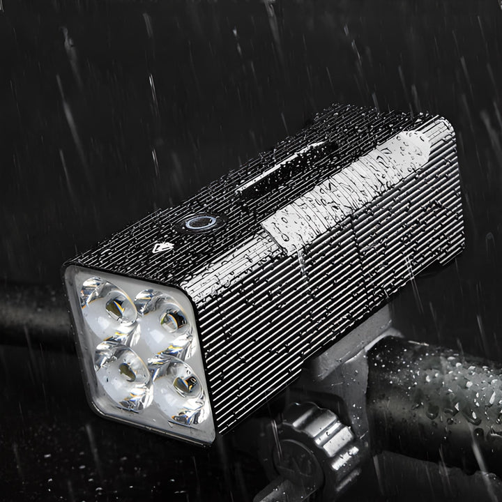 Wasserdichte LED-Fahrradleuchte, schwarz, mit vier Linsen, montiert auf Lenker im Regen.